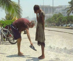 Elderly man giving his flip flops to a woman who has no shoes.